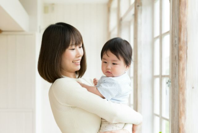 窓際に立つ赤ちゃんを抱っこした女性