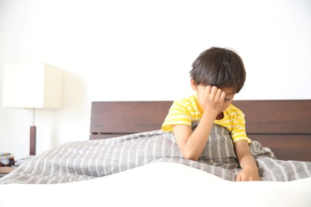 ベッドの上で頭に手を当てて下を向く男の子